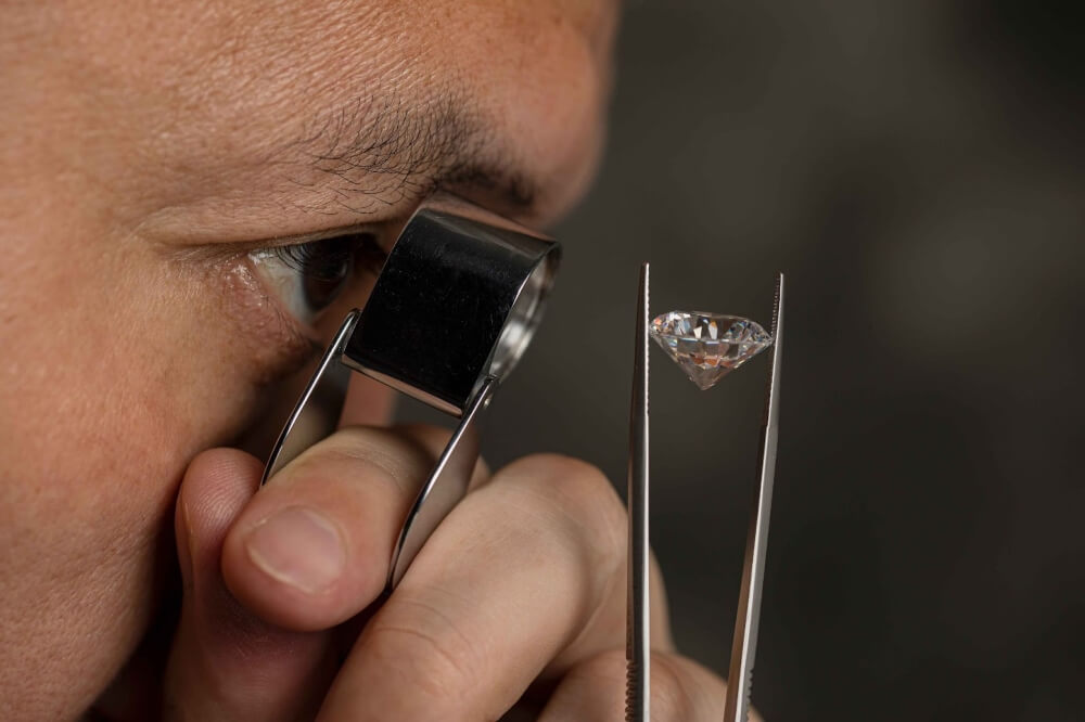 A man inspects a diamond using a pair of tweezers and a jeweler’s loupe.