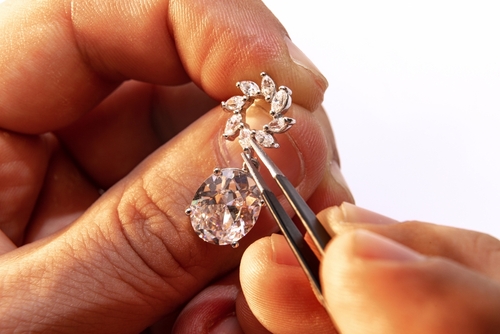 A close-up shot of a bench jeweler's hands repairing a diamond earring