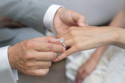 A groom slides a perfectly fitted diamond engagement ring onto a bride's finger