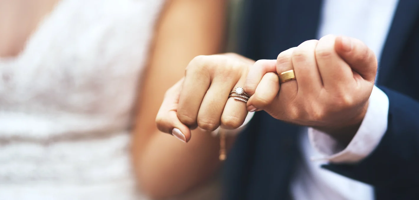 An close up image of the hands of a bride and groom with their pinky fingers linked together in a "pinky promise"