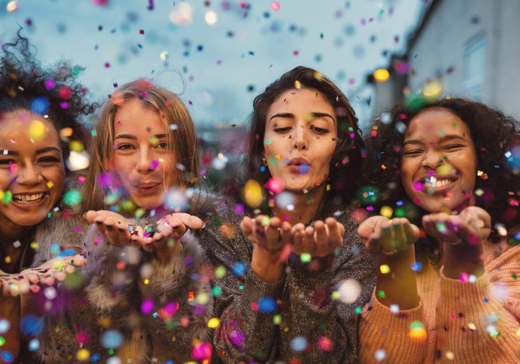 Young,Women,Blowing,Confetti,From,Hands.,Friends,Celebrating,Outdoors,In
