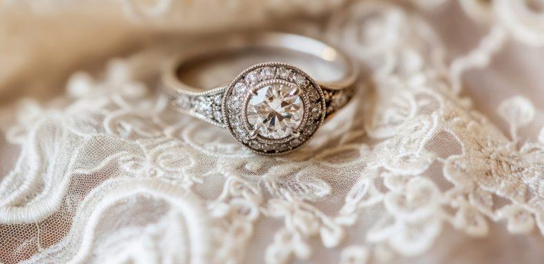 A close-up of a vintage-style diamond ring with intricate detailing, placed on a lace handkerchief.