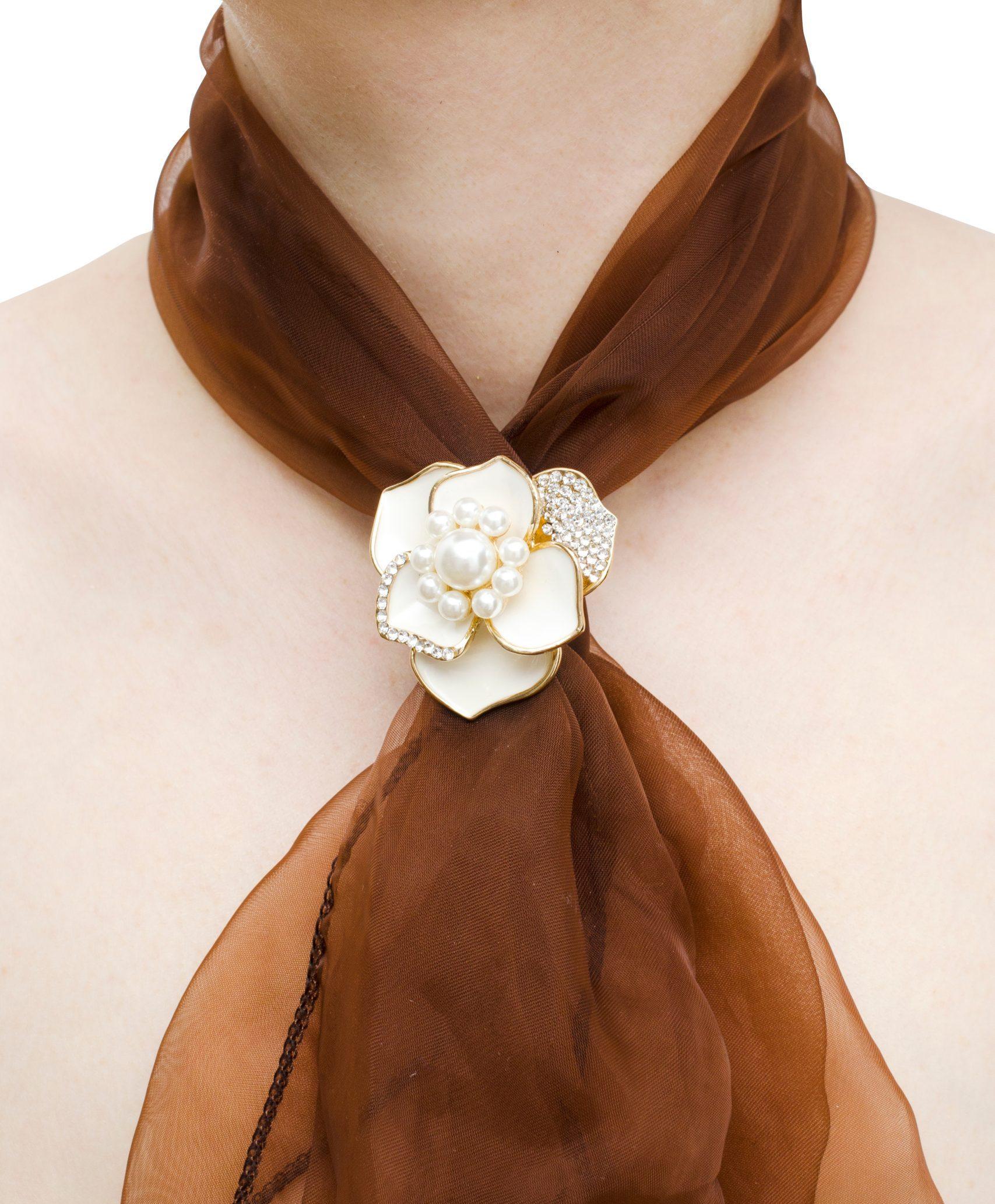 A white flower brooch holding a brownn scarf around a woman's neck