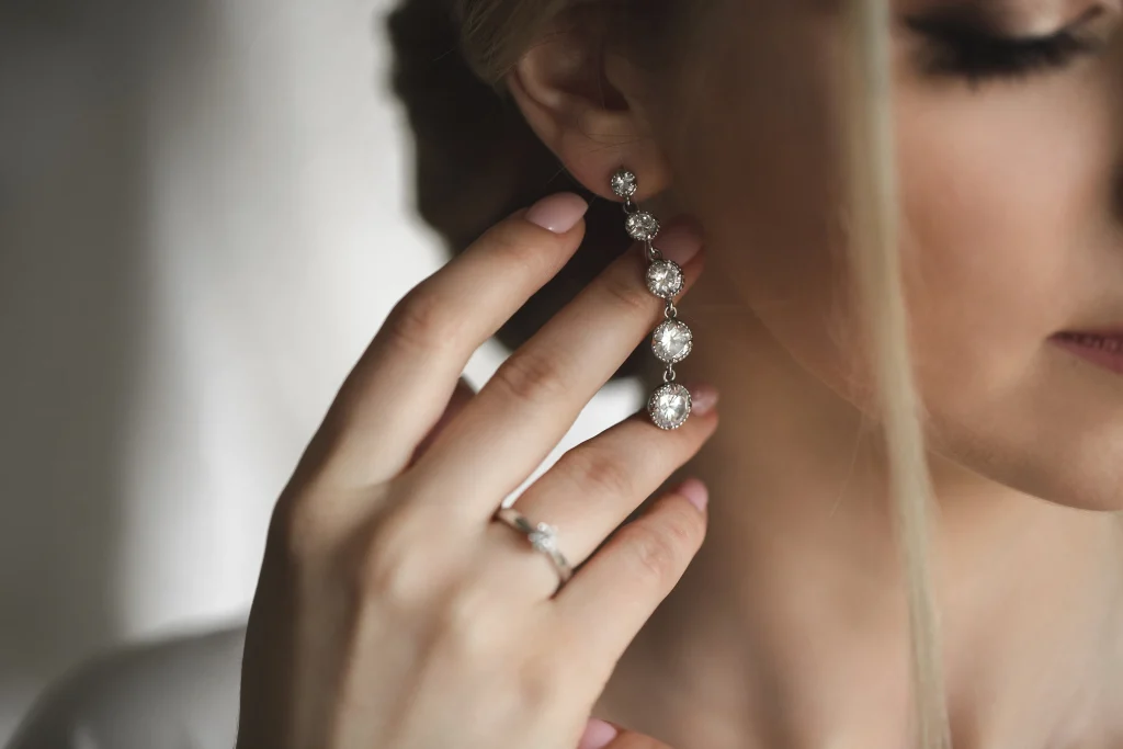 A woman delicately touching a diamond drop earring in her ear