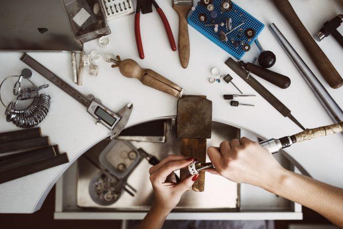 A jeweler's workbench used in jewelry repairs with a woman's hands polishing a silver ring with a grinding machine.