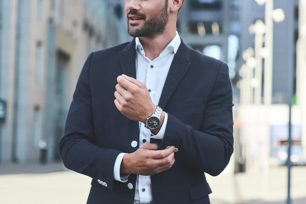 A man in a suit wearing a watch with a blurred city street behind him